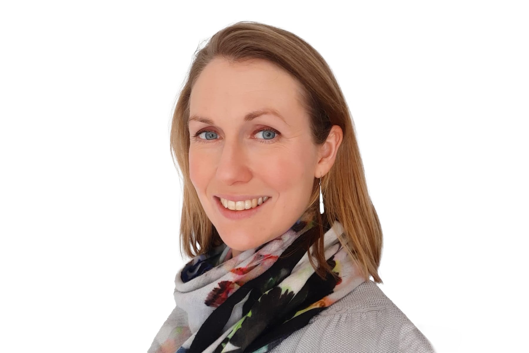 Rosie Dunscombe, a white woman with short blonde hair, smiling at the camera. She is wearing a floral scarf and a grey cardigan.